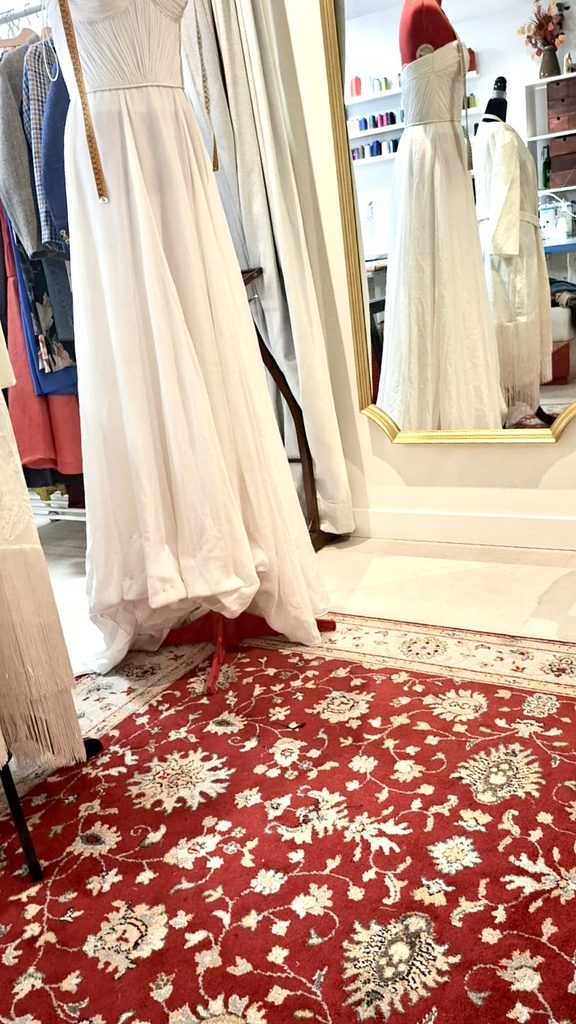 Vestido largo claro sobre un maniquí junto al espejo del atelier