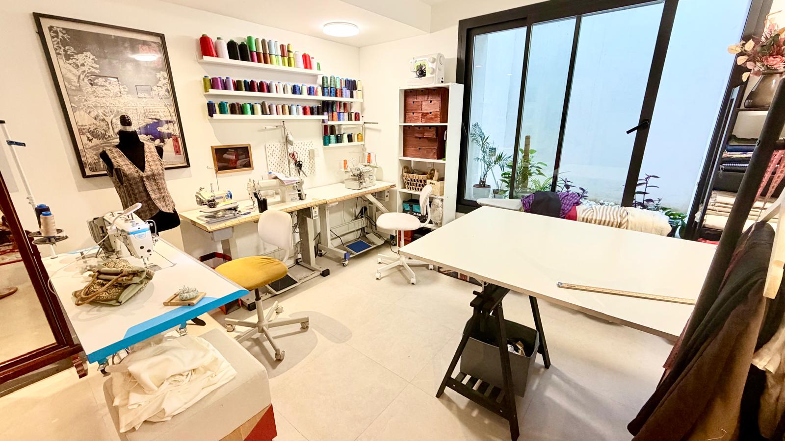 Vista del taller con mesas de trabajo, máquinas de coser y estanterías de hilos